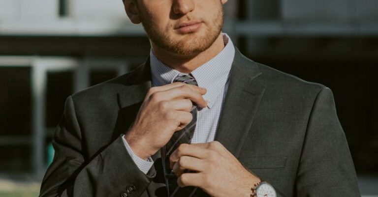 Thought Leader - Serious confident male entrepreneur wearing classy suit and wristwatch holding tie while thoughtfully looking away