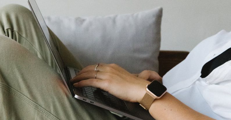 Employers - Side view of crop unrecognizable female freelancer in casual clothes and smartwatch lying on comfortable sofa and working remotely on laptop